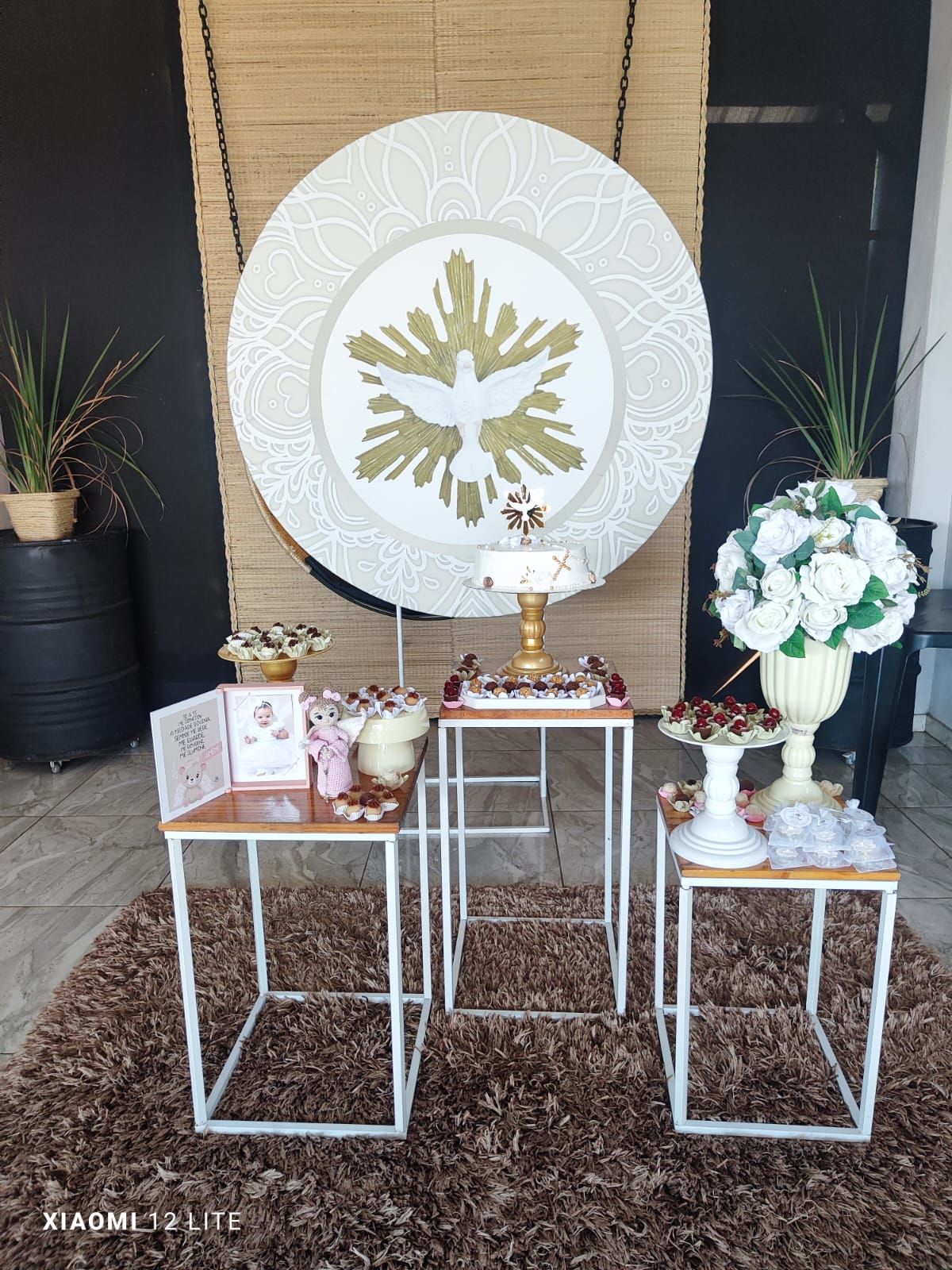 Decoração de batizado com painel redondo do Divino Espírito Santo, trio de mesas e arranjo de rosas brancas