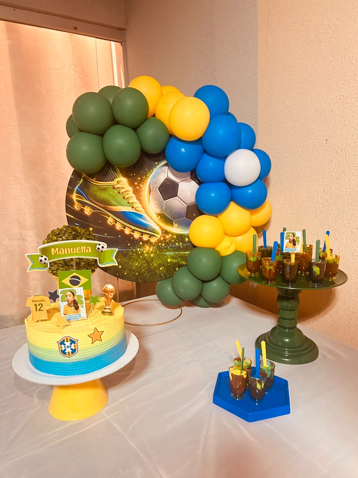 Kit montado no tema futebol/Brasil com arco de balões verde, amarelo e azul, painel de campo e bola — decoração infantil da Manuella 12 anos