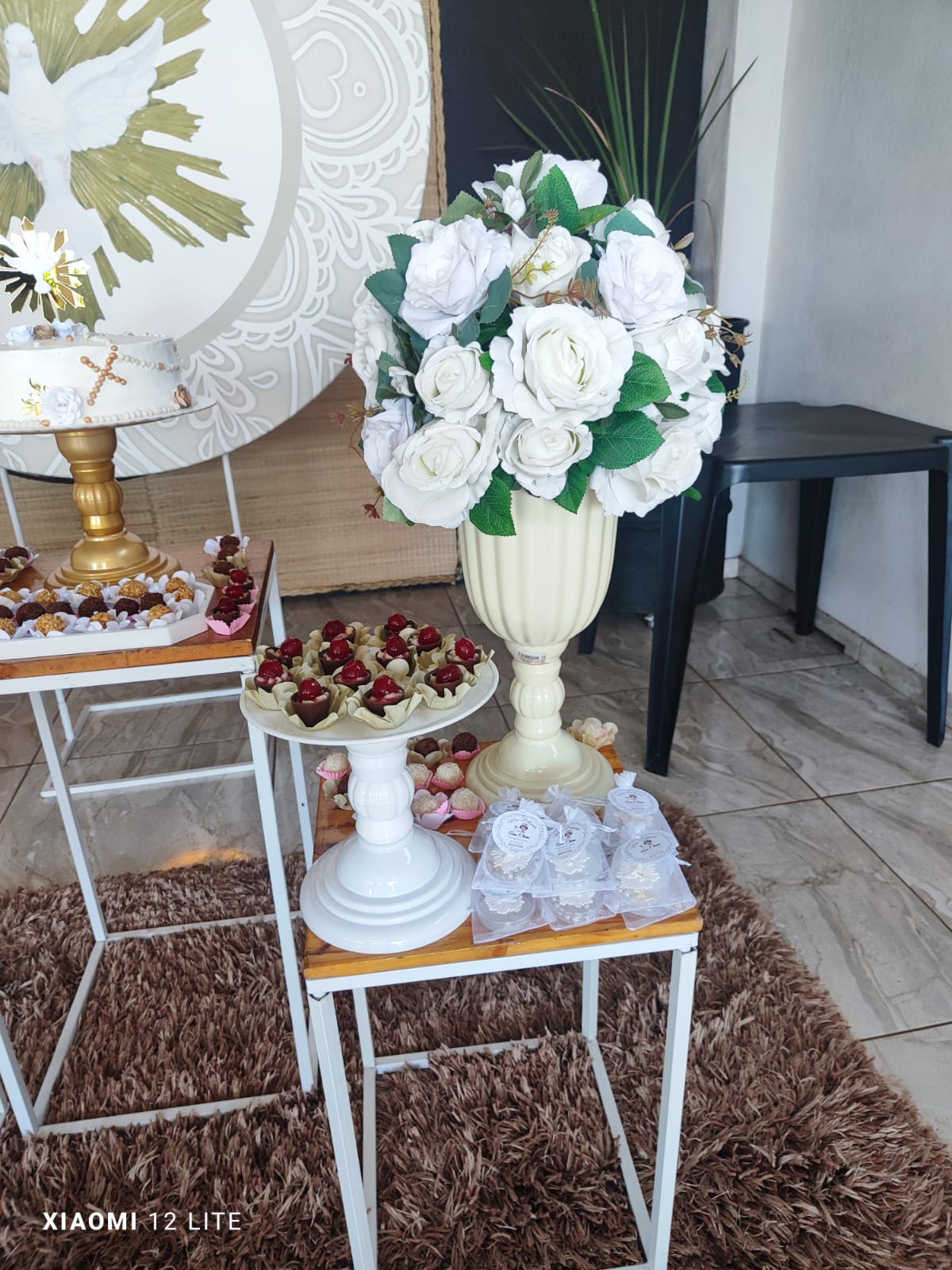 Trio de mesas de batizado com doces, lembrancinhas e vaso com rosas brancas