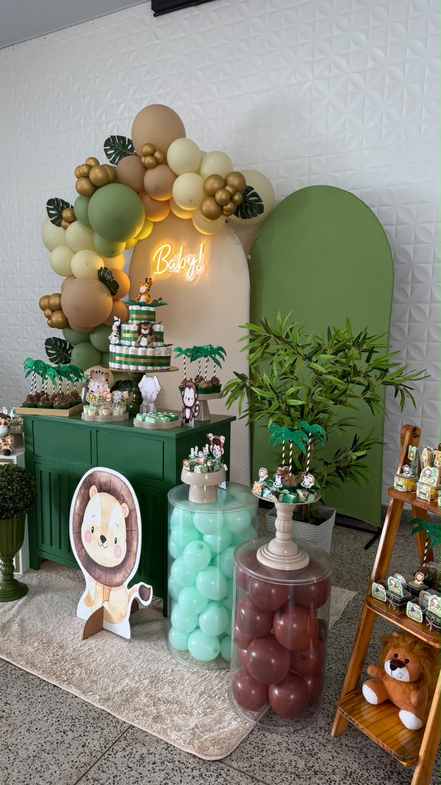 Decoração de chá de bebê tema safári com arco de balões verdes e dourados, neon Baby! e bolo de fraldas