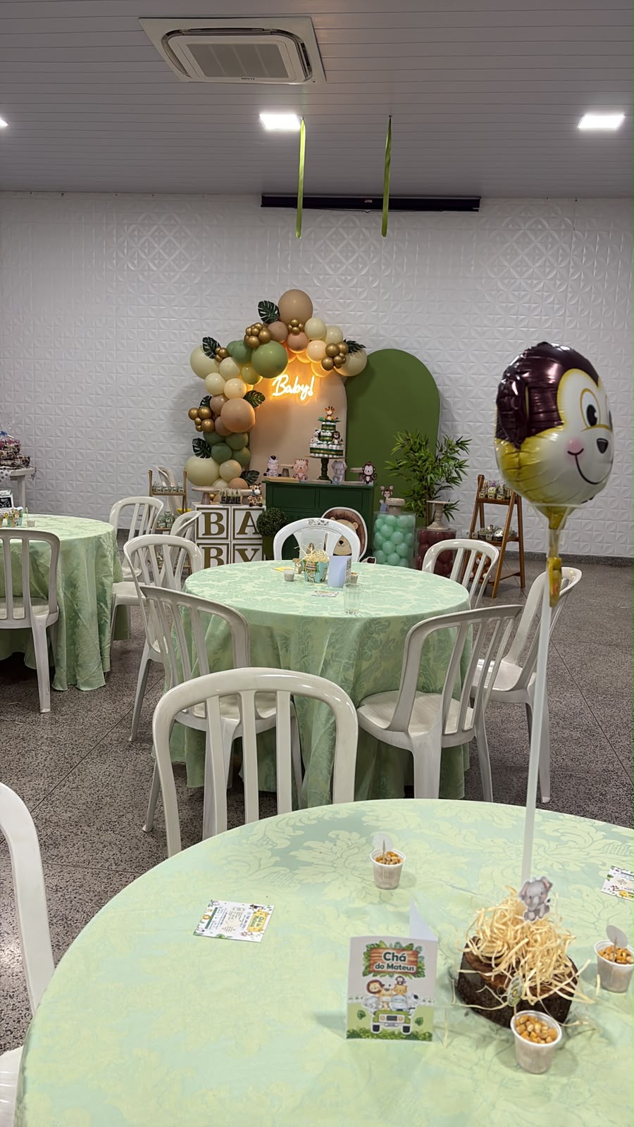 Salão decorado para chá de bebê com mesas redondas verdes e painel temático safári ao fundo